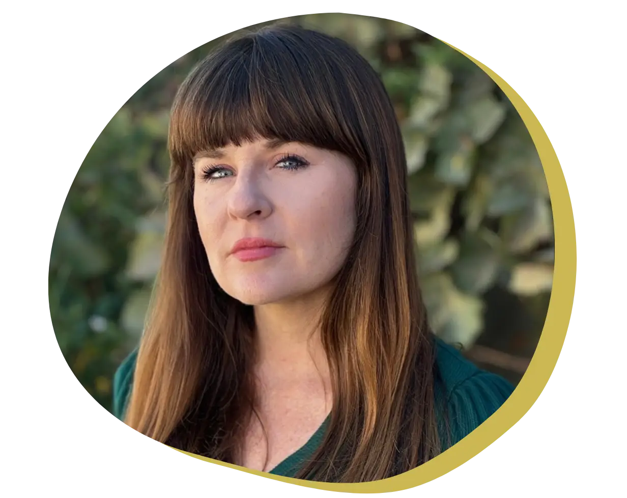 A woman with long brown hair and bangs is looking at the camera with a neutral expression. She is outdoors in front of greenery, and the image has a tan and yellow rounded border.